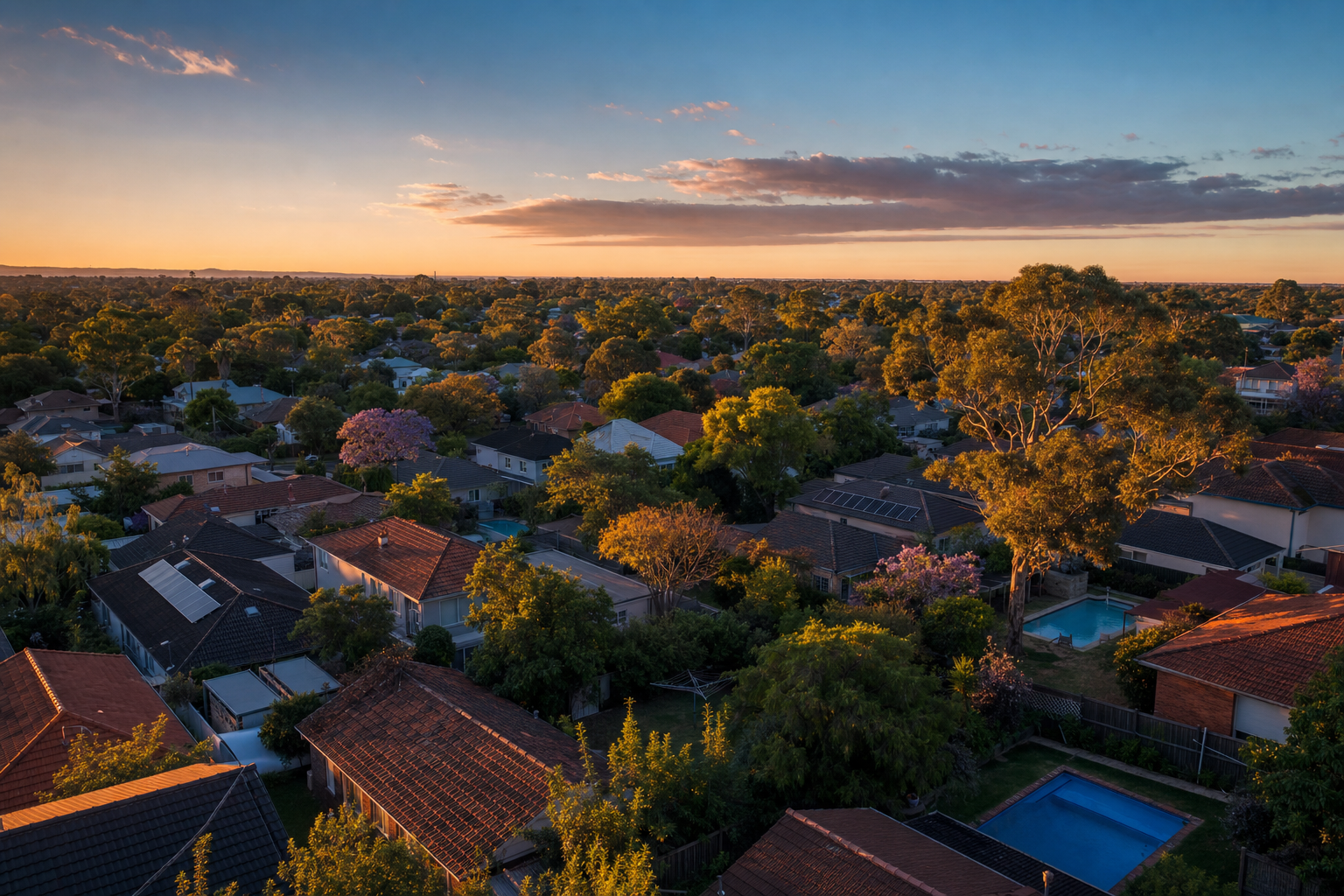 Aerial-oblique view of an Australian suburban rooftop line at late golden hour — terracotta tiled roofs, gum-tree and jacaranda canopies between them, deep blue evening sky — illustrating that the house stays, the path back exists.